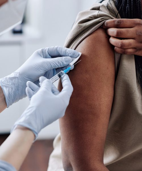 Close-up of nurse in protective gloves using syringe to vaccinate African girl at hospital